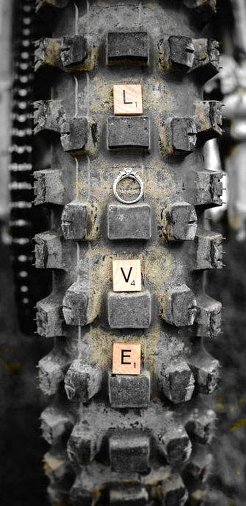 Diamond ring and Scrabble tiles spelling LOVE on the textured tread of a black off-road motorcycle tire.