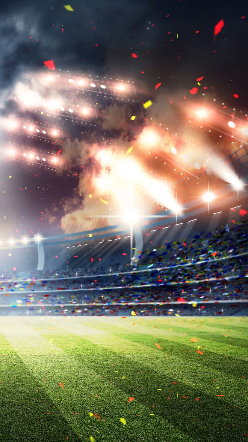 Bright stadium floodlights shine over a green soccer field with falling confetti under a dark evening sky.
