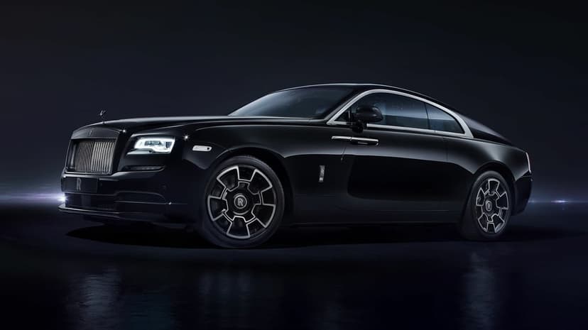 Side view of a black Rolls-Royce Wraith luxury car with chrome accents in a dark studio with dramatic lighting.