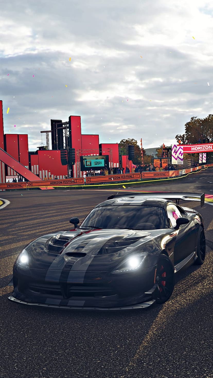 Black Dodge Viper with racing stripes speeds past red festival banners and confetti on a night racing circuit.