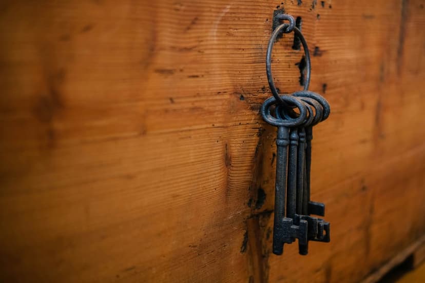 Antique skeleton keys hang from a heavy iron ring against a weathered wooden chest showing rusted metal textures.