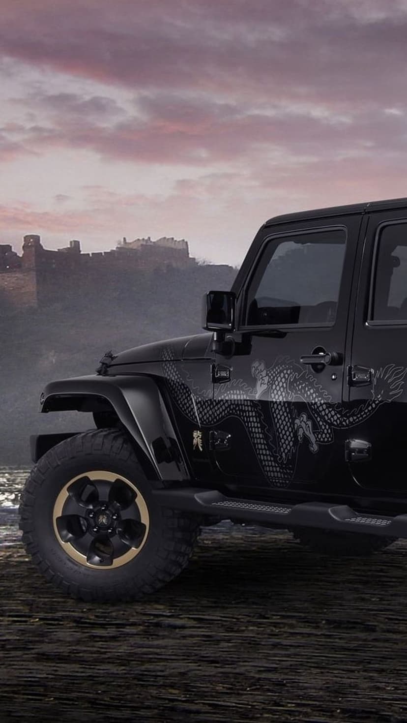Black Jeep Wrangler with dragon decals parked in front of a medieval stone castle under a purple evening sky.