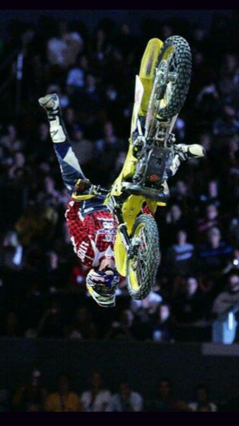 Motocross rider in red gear flips a yellow motorcycle upside down mid-air during a stadium competition event.