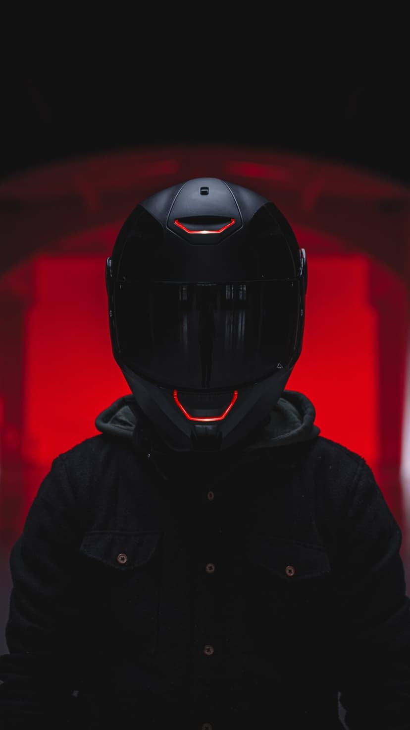 Cyberpunk rider wearing a black helmet with red LED accents against a blurred crimson tunnel background.