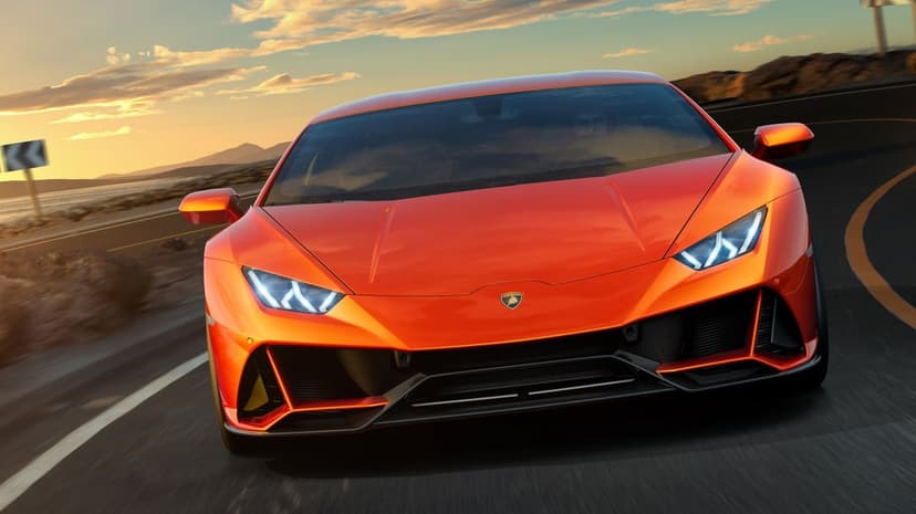 Orange Lamborghini supercar driving on a winding road at sunset with motion blur and golden sky.