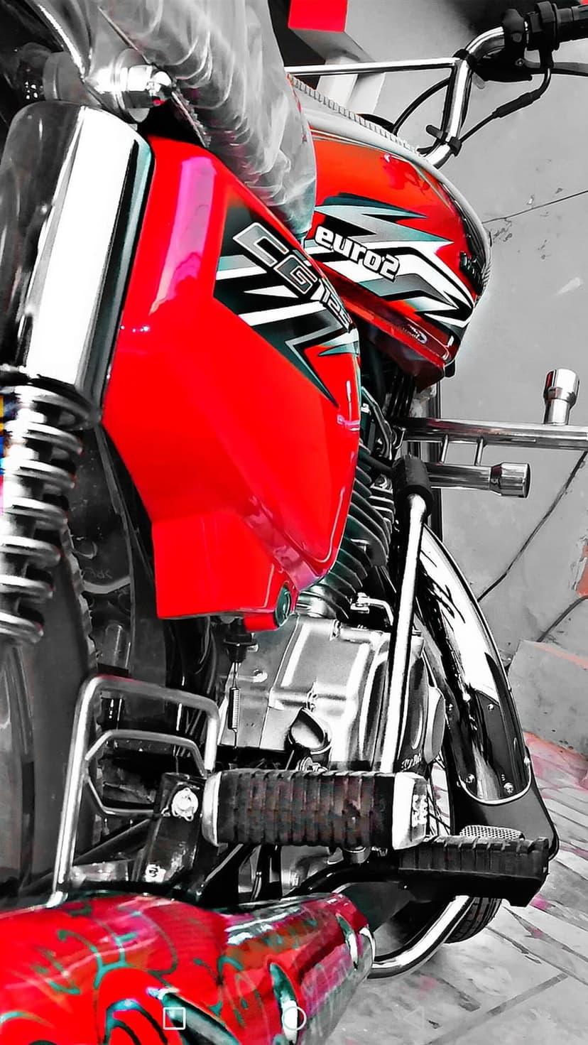 Red Honda CG 125 motorcycle front view with chrome handlebars and a fuel tank on a grayscale background.