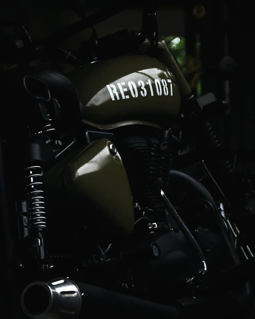 Olive green motorcycle fuel tank with white decal above a dark metallic engine and textured suspension.
