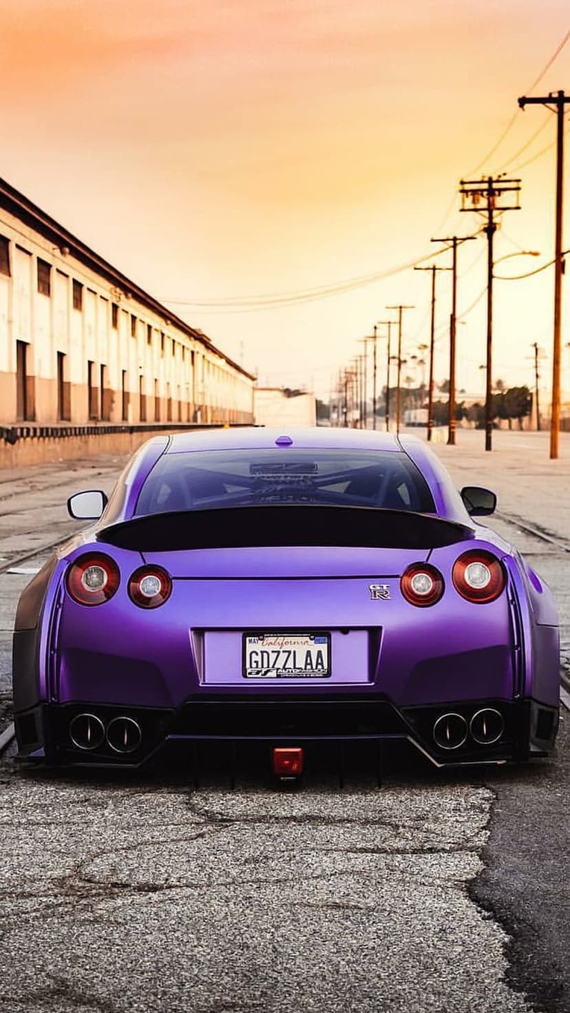 Purple Nissan GT-R with circular taillights and a spoiler parked on an industrial road under an orange sky.