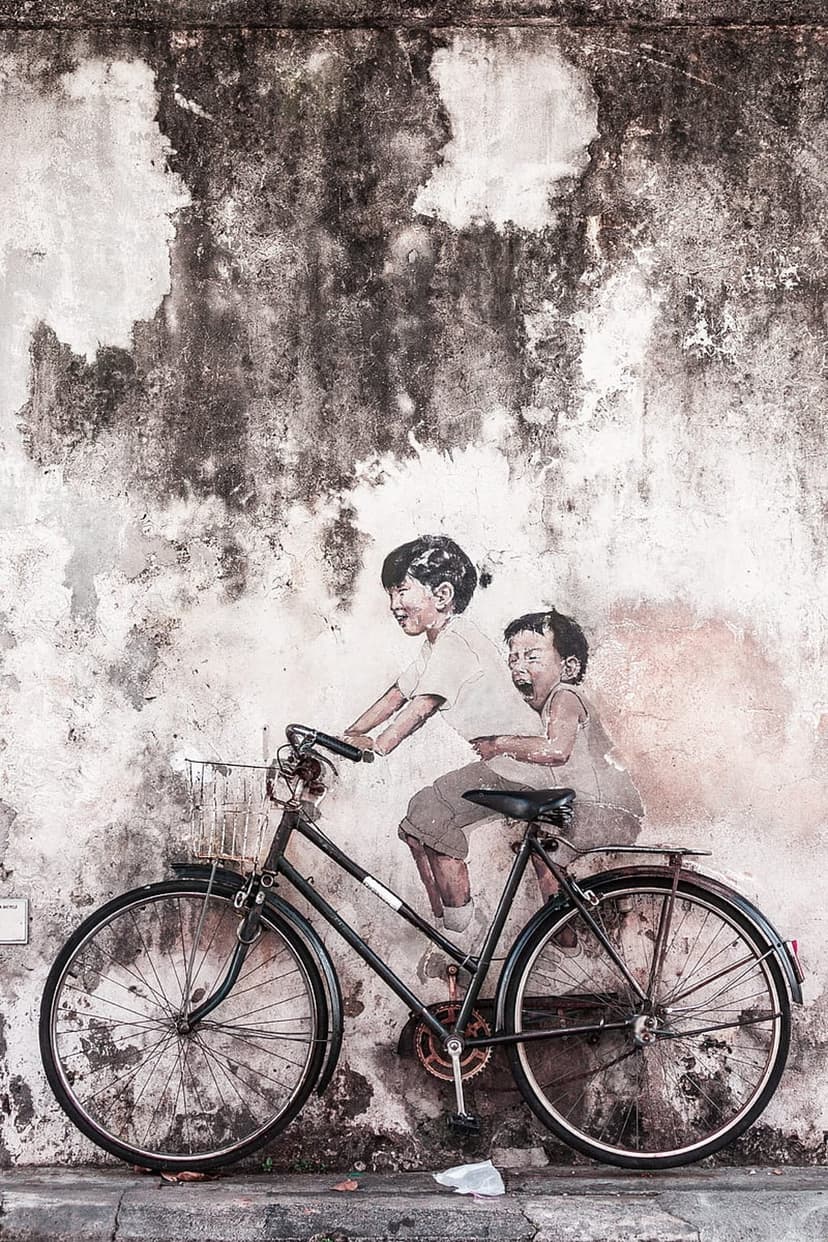 Two children ride a bicycle in a street art mural on a cracked, weathered wall with visible texture and peeling paint.