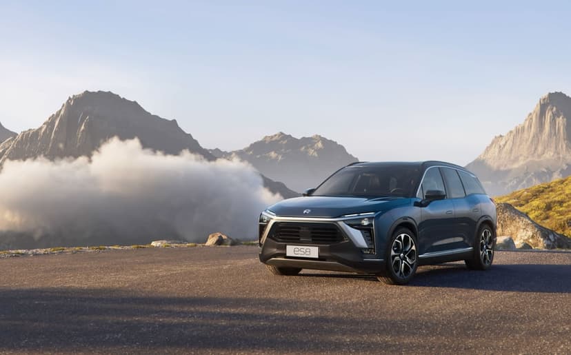 Dark blue NIO ES8 SUV parked on a paved road overlooking misty mountains and jagged peaks under a clear sky.