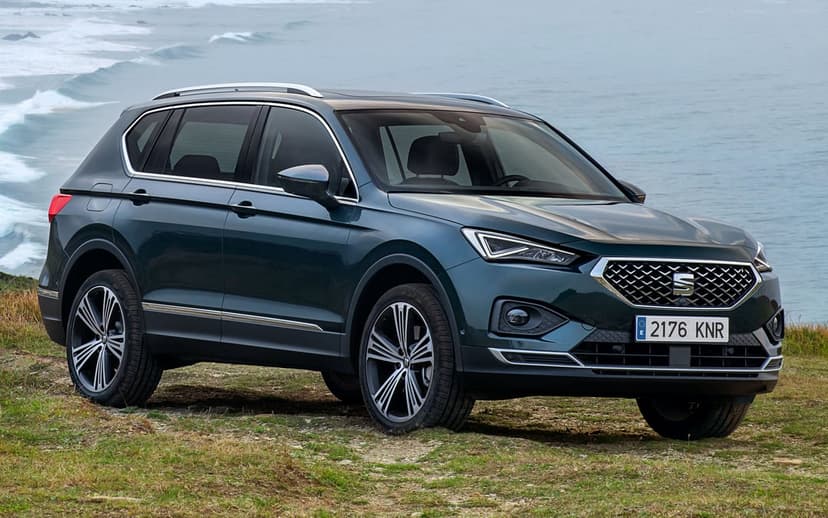 Dark green SEAT Tarraco SUV parked on a grassy cliff overlooking a misty ocean with crashing waves.