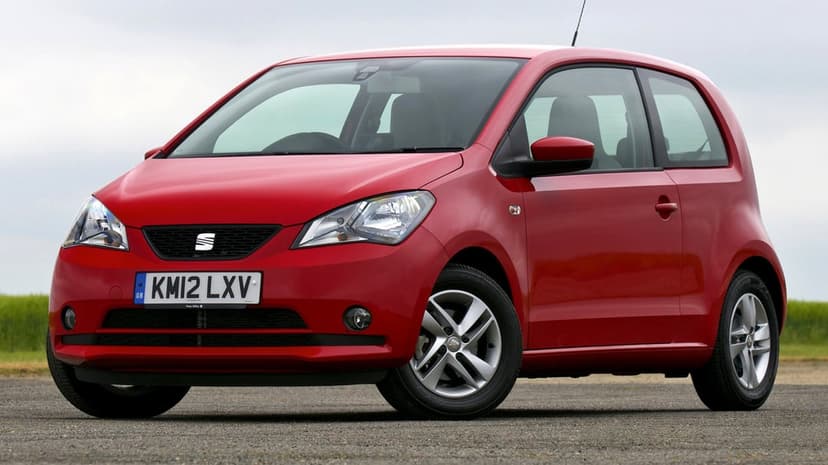 Red three-door SEAT Mii hatchback parked on gravel under a cloudy sky in a professional studio style.