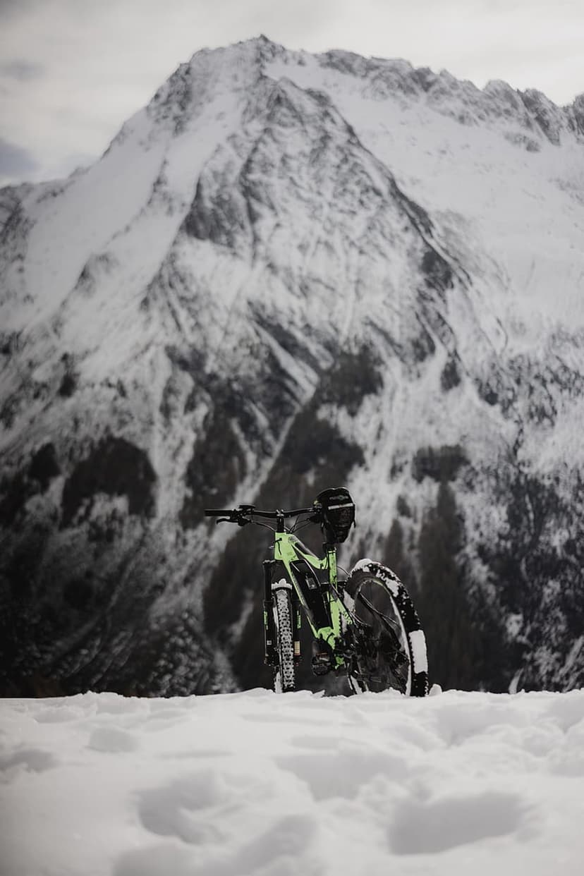 Neon green fat bike parked in deep white snow with massive jagged mountains under a clear winter sky.