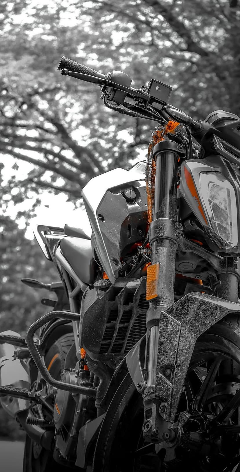 KTM motorcycle handlebars and front suspension with orange accents on a black and white blurred street background.