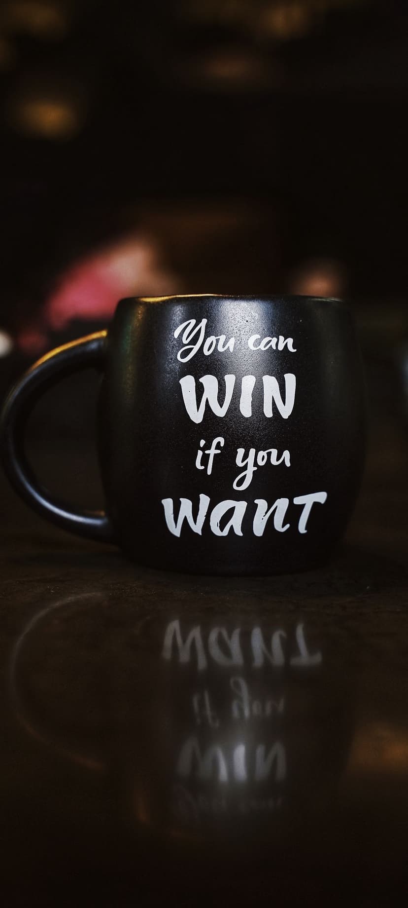 Black ceramic mug with You can WIN if you want text in white script on a dark reflective surface.