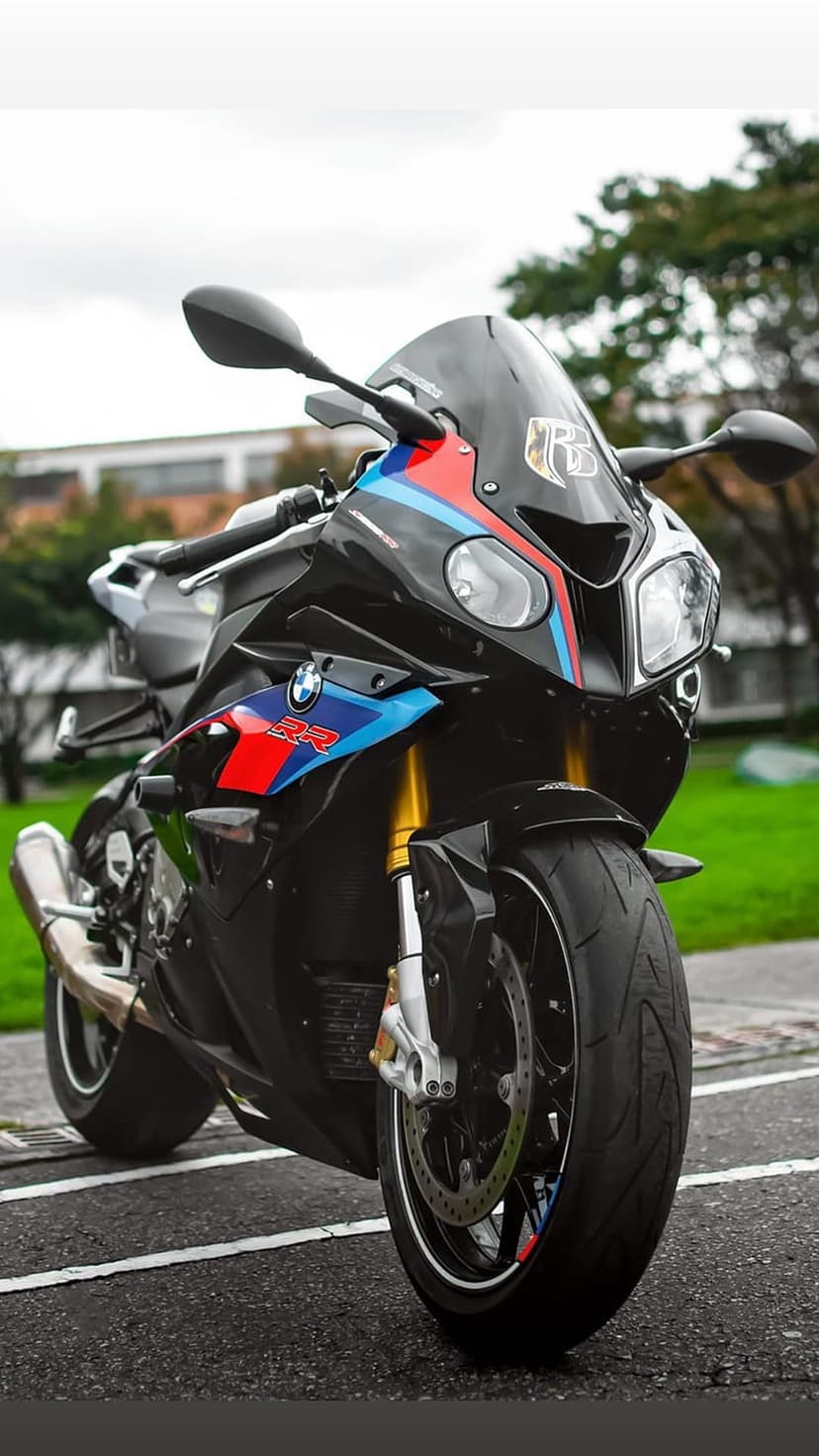 Black BMW S1000RR motorcycle with tricolor M Sport stripes, gold front forks, and a silver exhaust on asphalt.