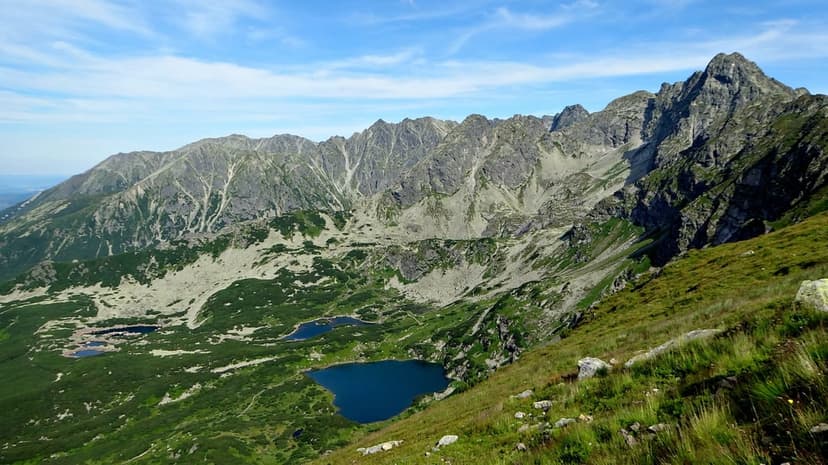 Jagged granite peaks overlook deep sapphire alpine lakes within a lush green valley under a clear blue sky.