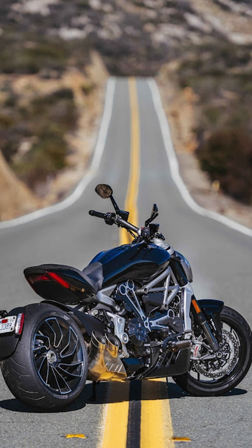 Black motorcycle parked on a winding asphalt road with double yellow lines leading toward hazy distant hills.