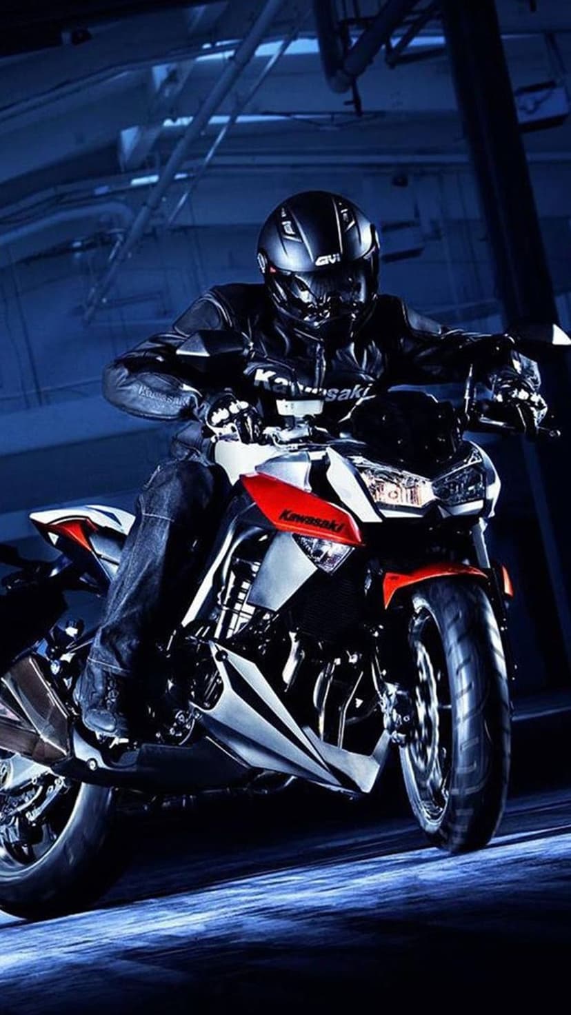 Motorcyclist in black leather gear sits on a Kawasaki bike featuring red accents under moody blue industrial lights.