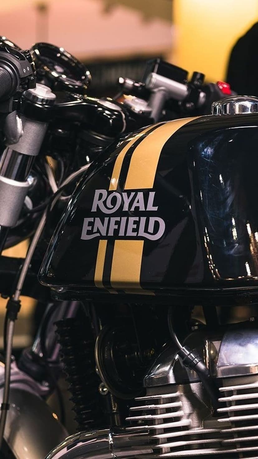 Black Royal Enfield fuel tank with gold pinstripes, silver logo, and polished chrome engine components.