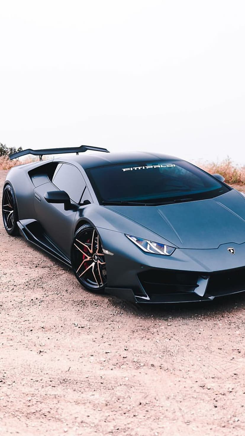 Matte gray Lamborghini Huracan with a large rear wing and custom gold rims parked on a rural dirt road.
