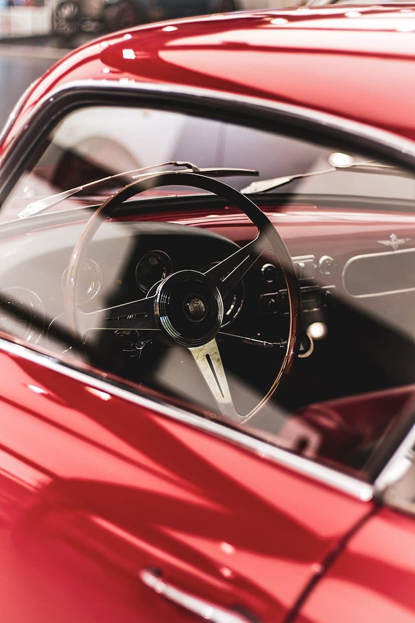 Classic red car steering wheel and dashboard with glossy reflections on the polished crimson exterior paint.