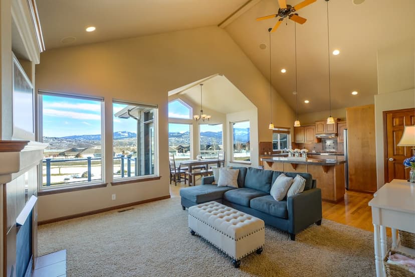 Charcoal sectional sofa and modern kitchen beside large windows overlooking a distant mountain range.