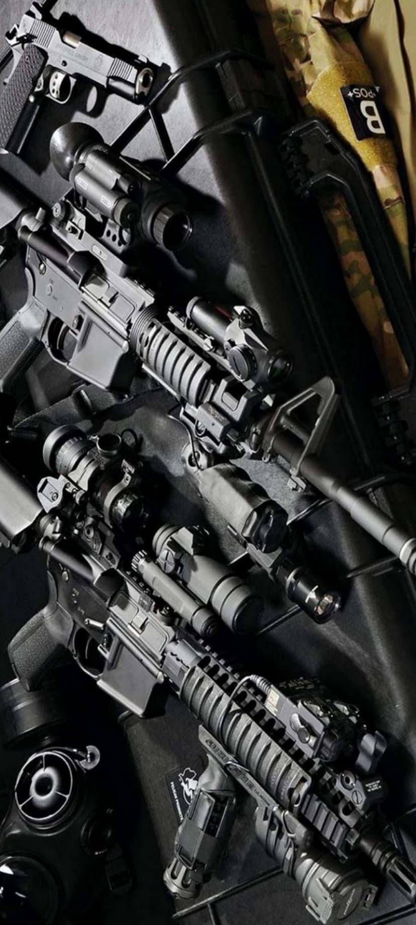 Specialized carbines and a pistol with optics sit inside a foam-lined hard case near a black gas mask.