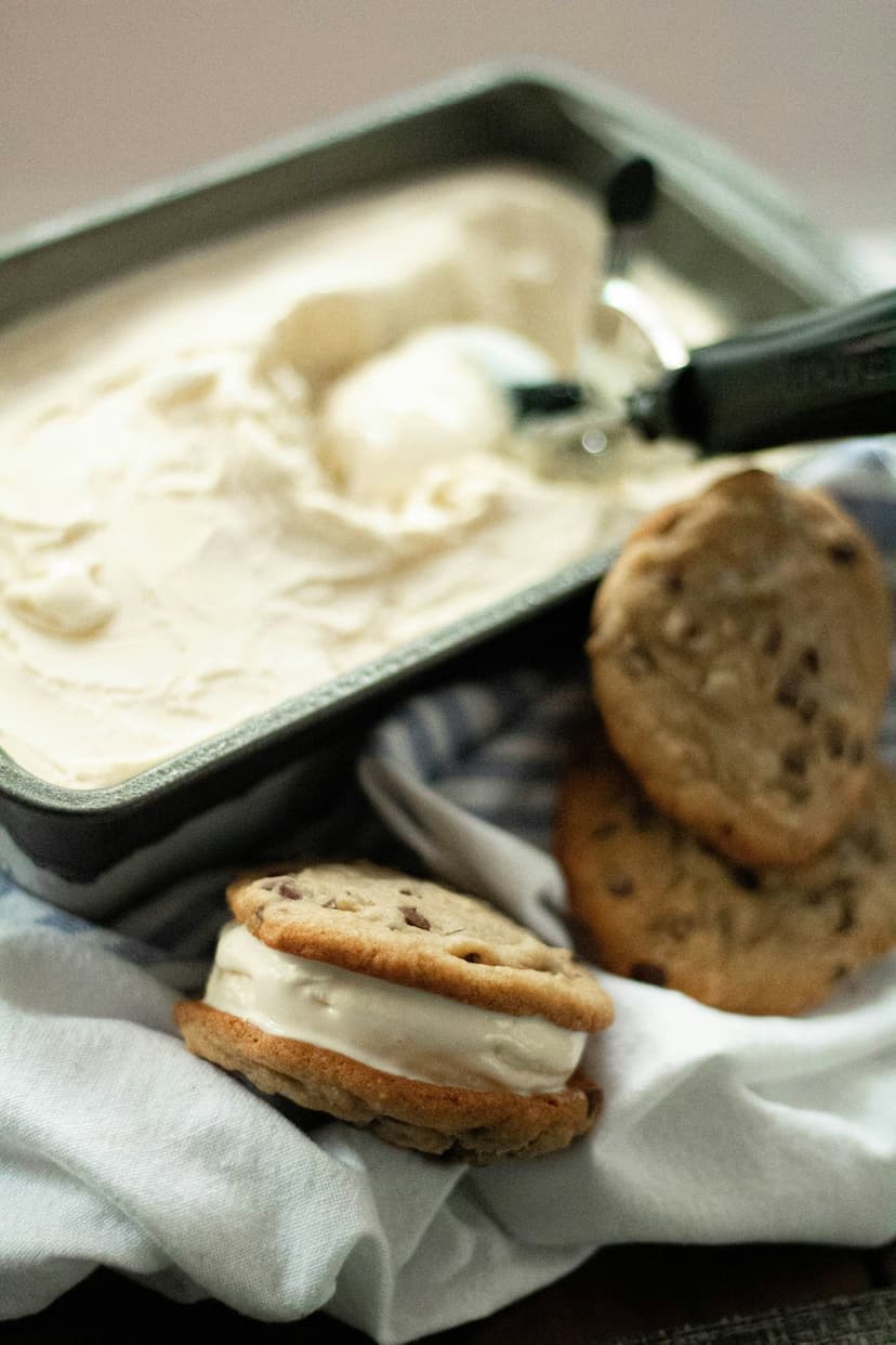 Chocolate chip cookie ice cream sandwich with melting vanilla center and visible chocolate chunks on a neutral plate.