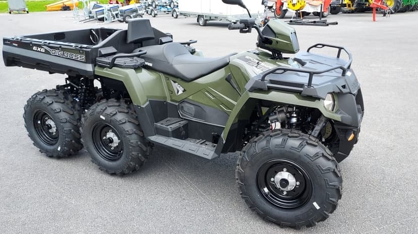 Olive green six-wheeled Polaris Big Boss ATV parked on asphalt with a rear cargo bed and knobby tires.
