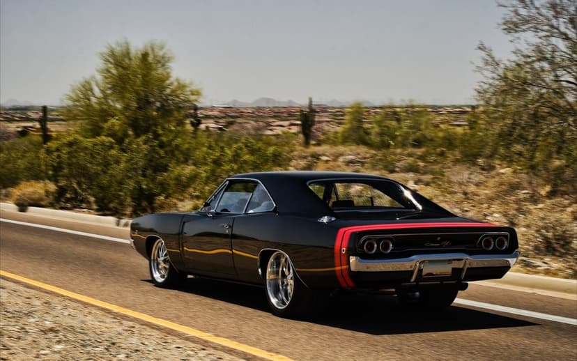 Black 1968 Dodge Charger R/T with red bumblebee stripes cruising along a sunlit desert road with motion blur.