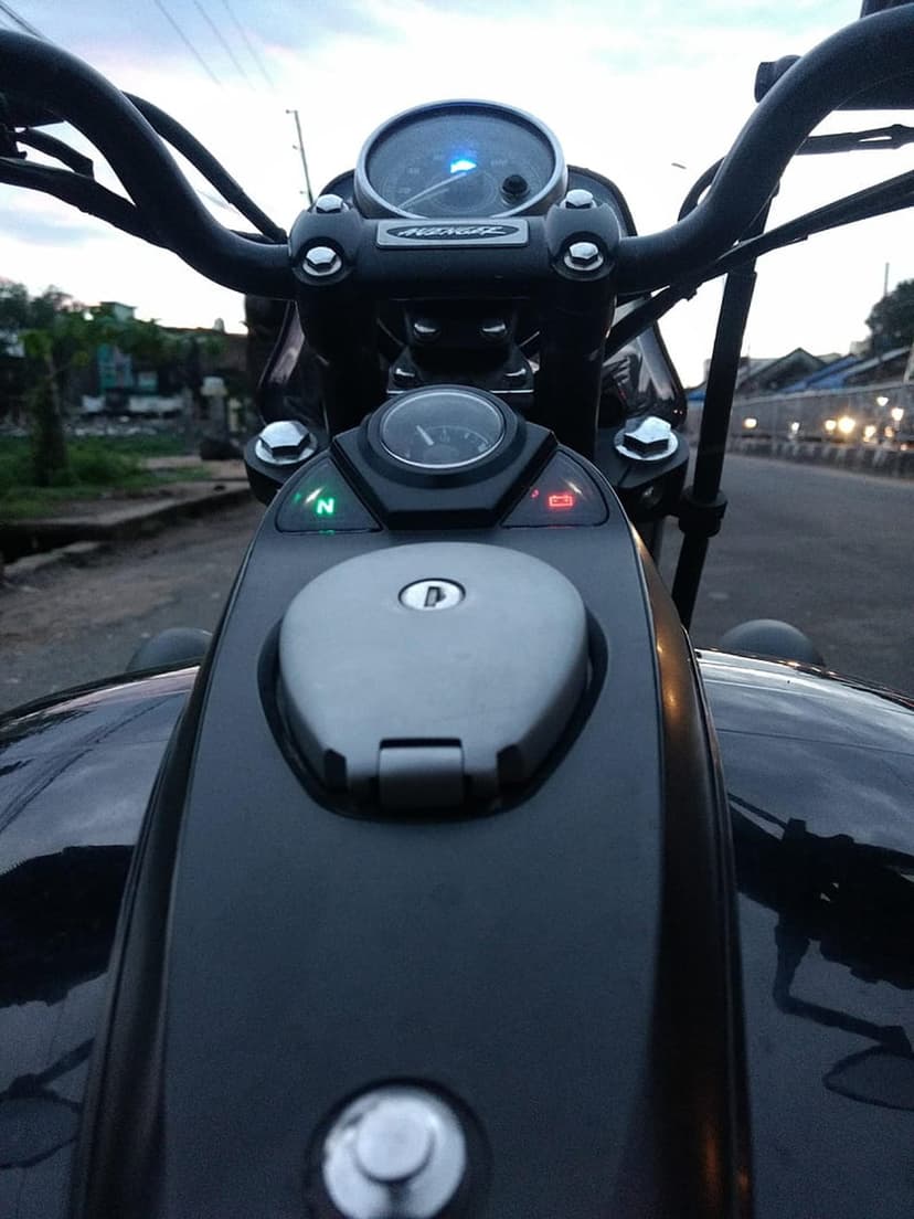 Motorcycle speedometer glows blue next to chrome handlebars and a glossy fuel tank during the evening twilight.