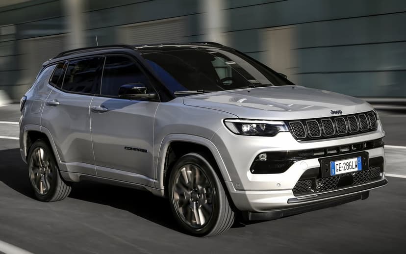 Silver Jeep Compass SUV driving on a road with motion blurred wheels and a grey urban building background.