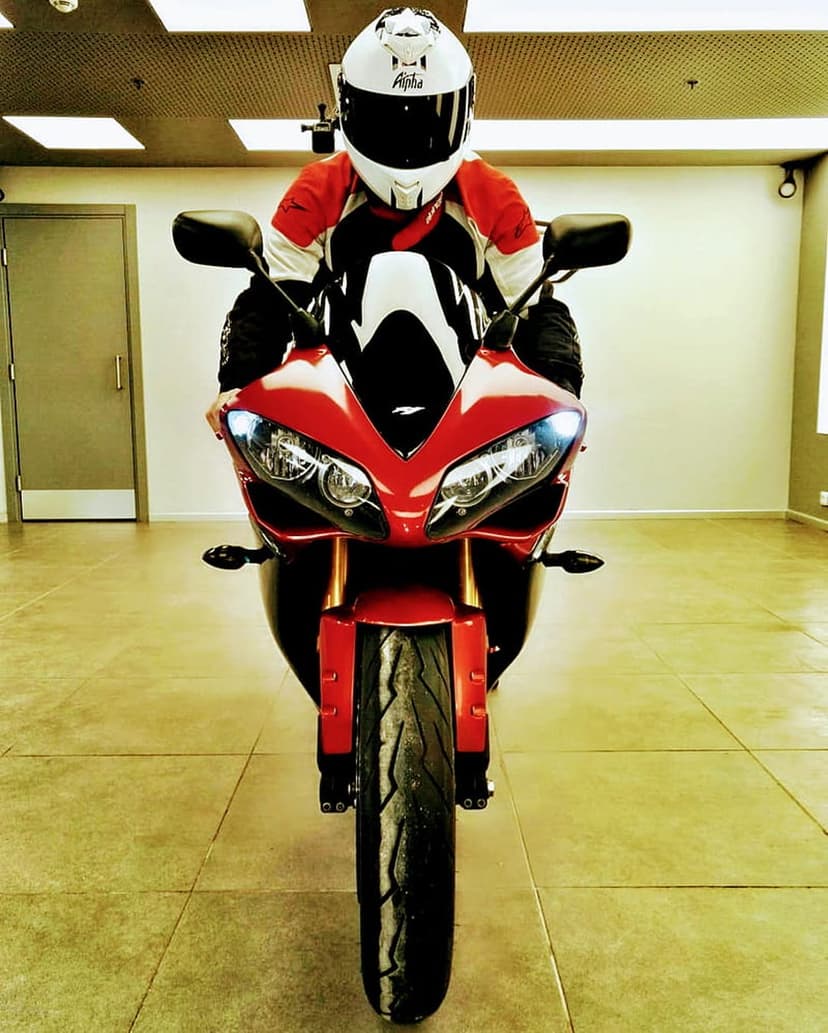Motorcyclist in a white and red helmet sits on a red sportbike over a tiled floor in a vertical composition.