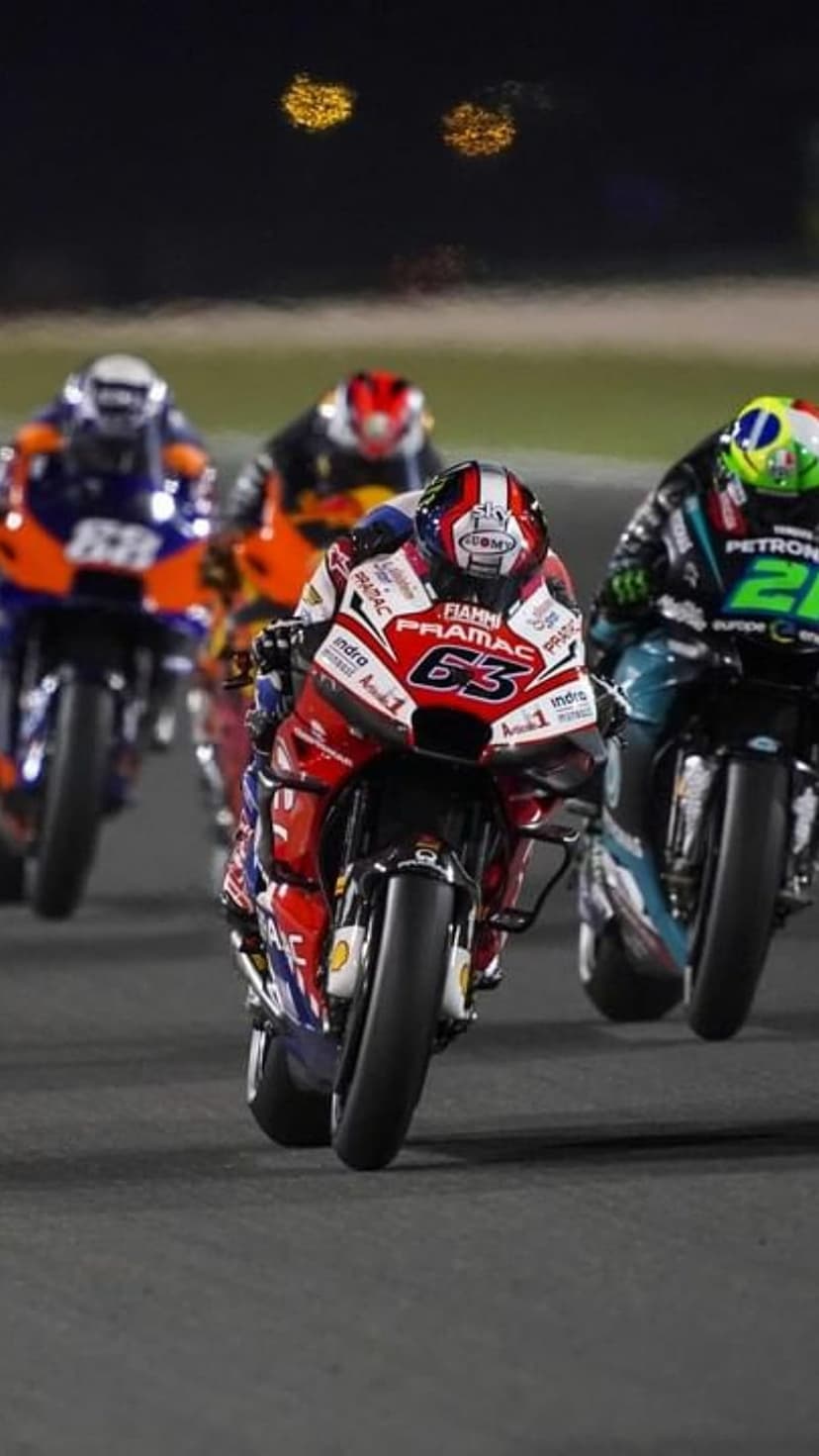 Professional motorcycle rider wearing number 63 leans into a turn on a lit circuit at night during a race.
