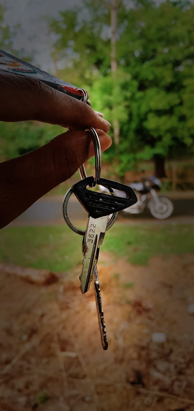 Hand holding motorcycle keys with a blurred bike in the background, showing sharp metallic textures and bokeh.