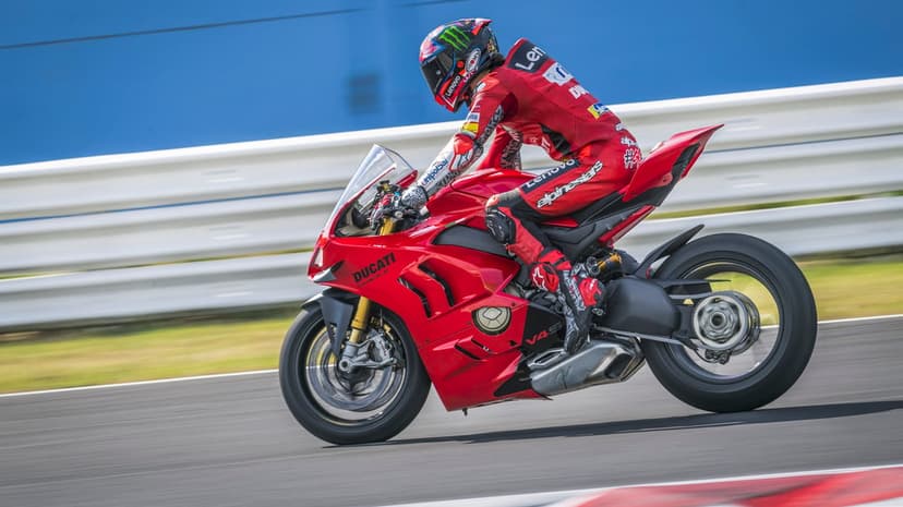Red Ducati Panigale V4 S racing on a track with a rider in red gear against a blue wall background.
