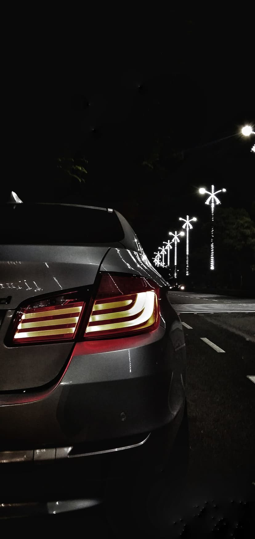 Red and yellow car taillights reflect on a wet dark surface under star-shaped white streetlights at night.