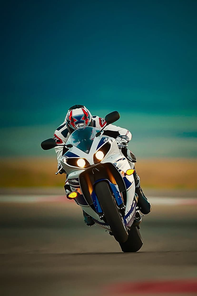 Motorcyclist in a blue and white racing suit leans a Yamaha sportbike into a turn on a blurred race track.