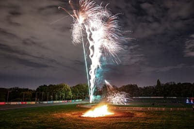Fireworks explode over a bonfire at night