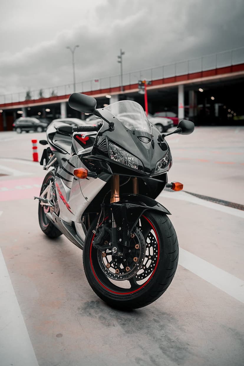 Black sportbike with red rim accents parked on concrete under a cloudy sky next to a modern urban building.