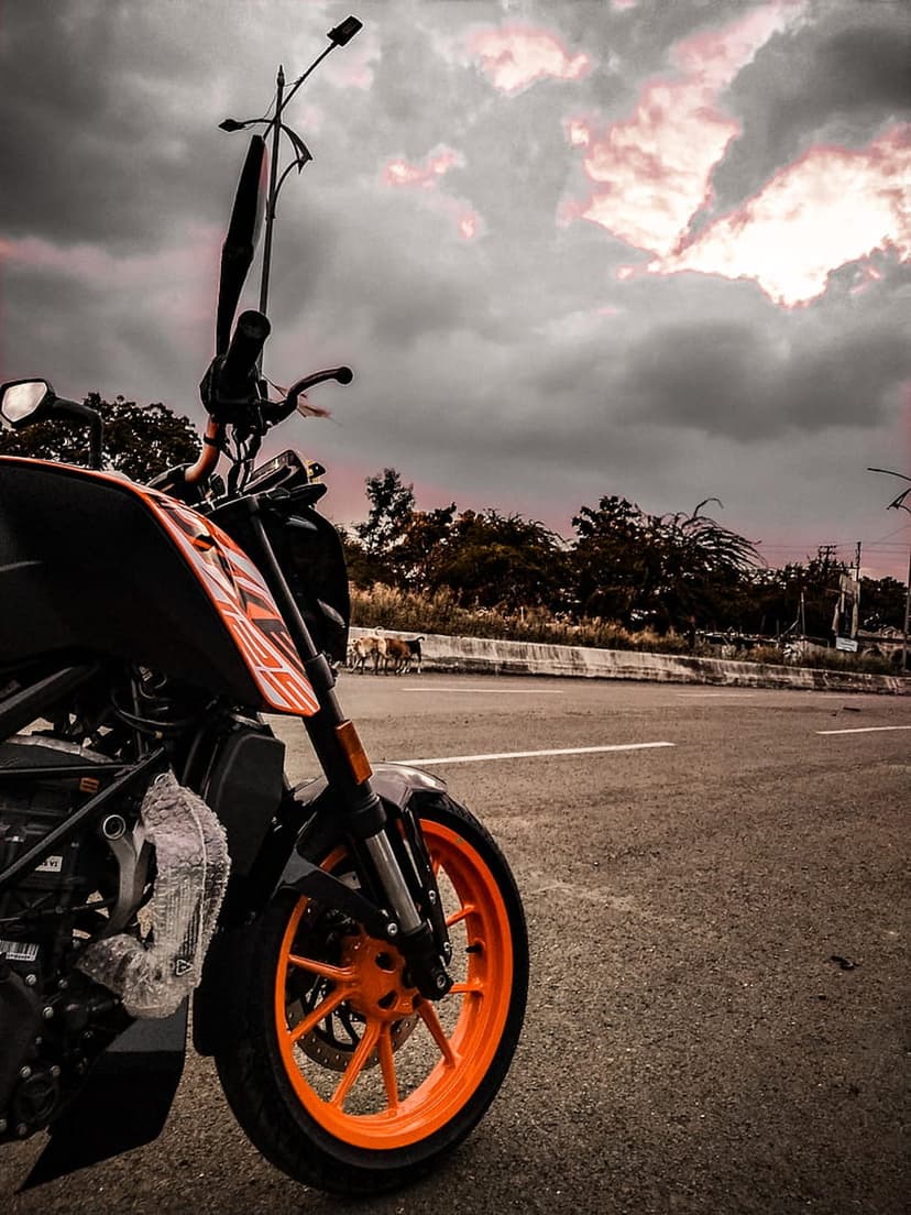 KTM motorcycle with orange rims and black bodywork parked on an asphalt road under a dark, cloudy sky.