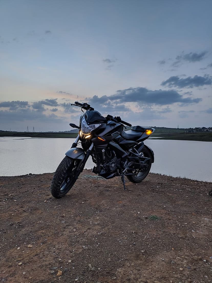 Black motorcycle parked on a dirt bank overlooking a calm lake under a cloudy blue and gray twilight sky.