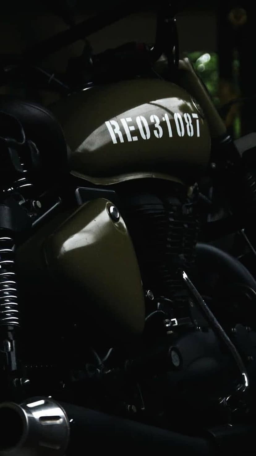 Royal Enfield motorcycle fuel tank in matte olive green with white stencil markings and dark moody lighting.