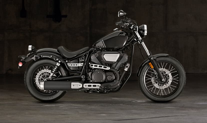 Side view of a black Yamaha Bolt motorcycle with silver accents against a dark textured concrete wall.