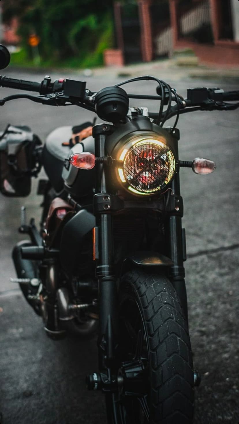 Circular motorcycle headlight with a metal mesh cover and amber signals on a custom black cafe racer.