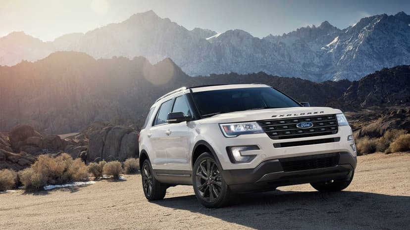 White Ford Explorer SUV on a dirt road with snow-capped mountains and sun flare in the background.