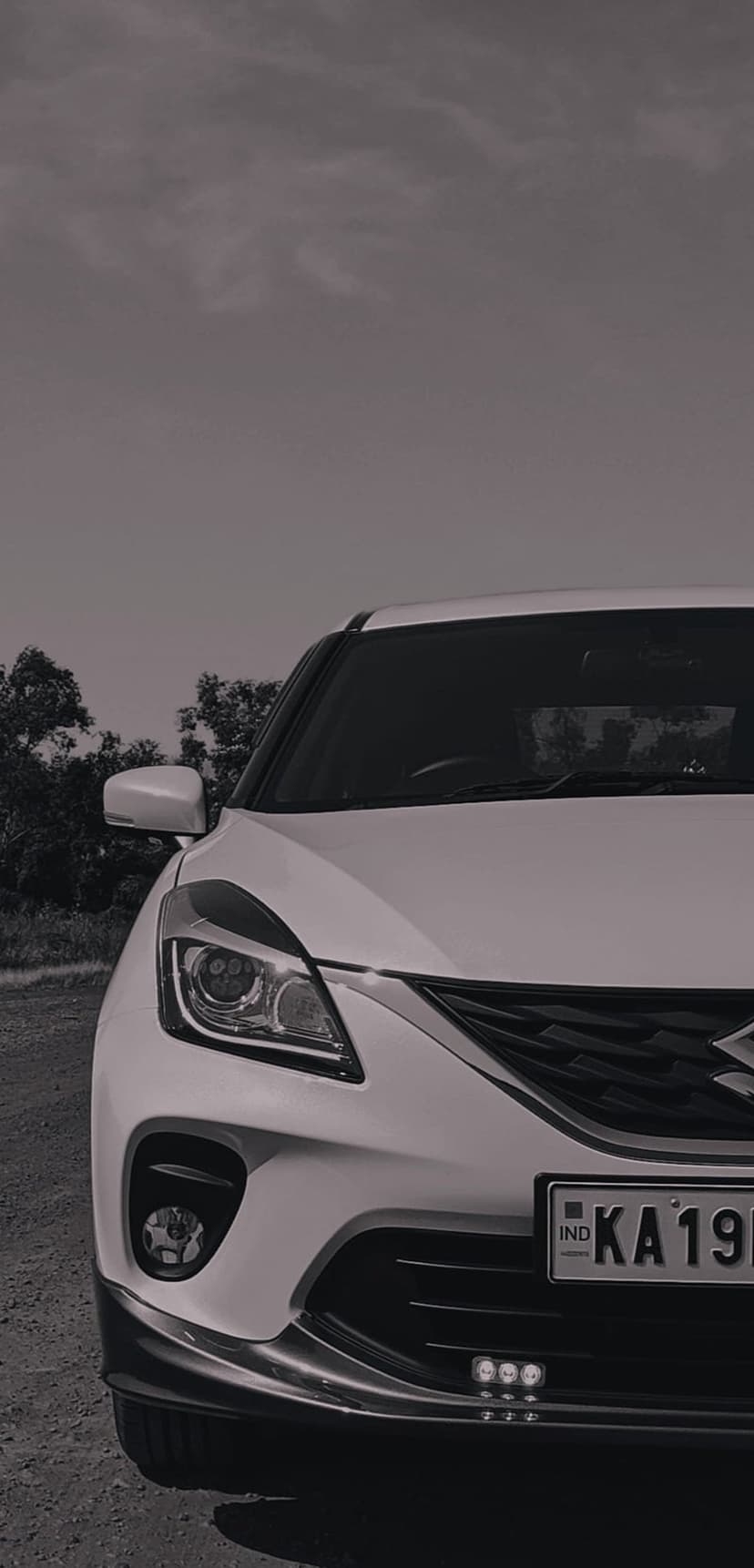 Maruti Baleno front grille and sharp headlights feature in a high-contrast black and white outdoor portrait.