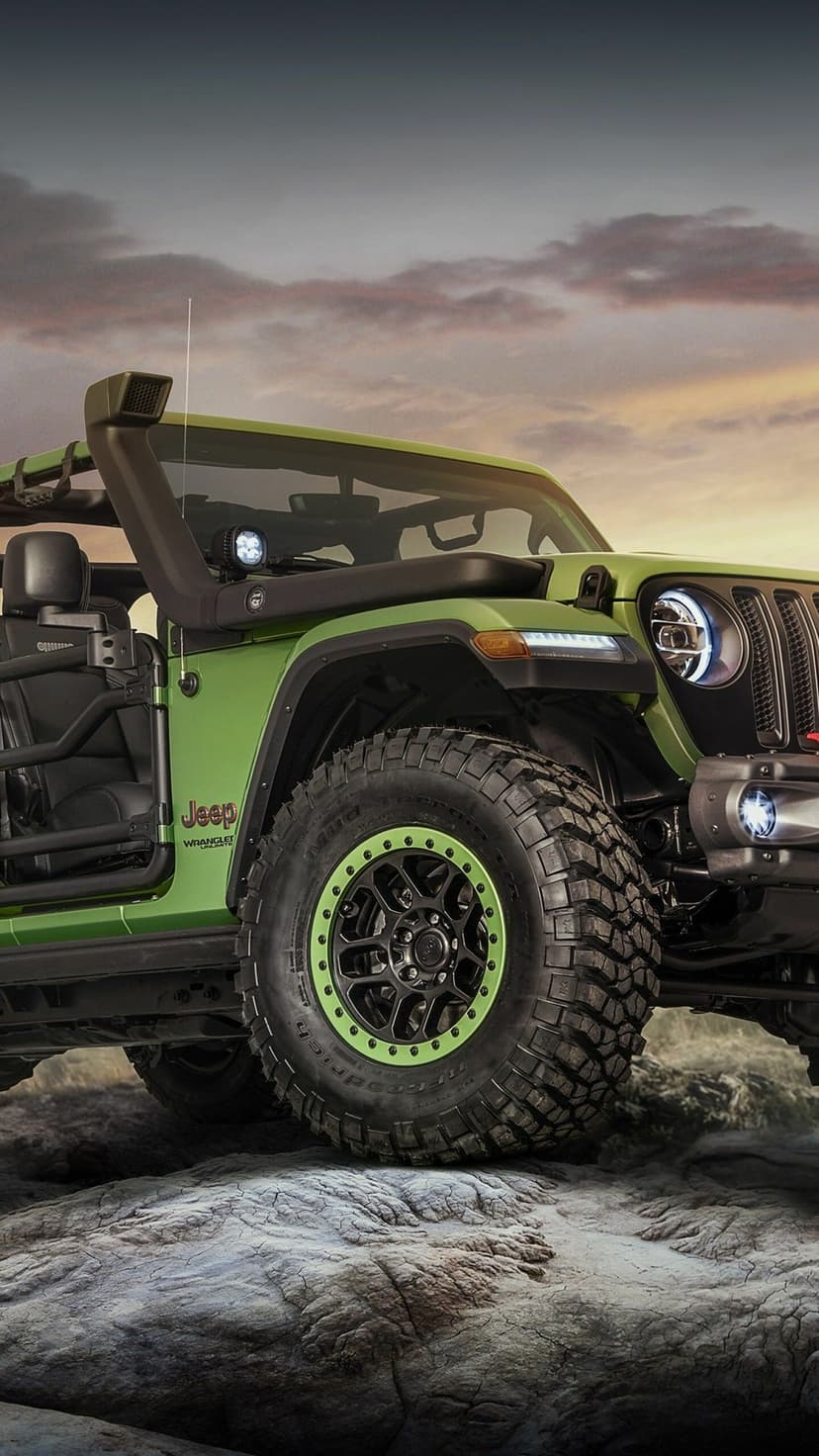 Lime green Jeep Wrangler with off-road tires and snorkel on a rocky hill under a colorful sunset sky.