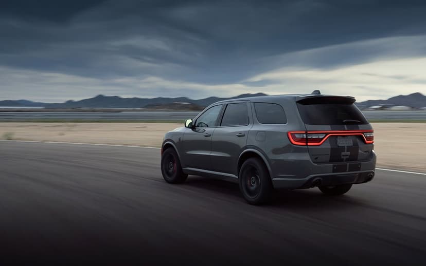 Grey performance SUV racing on a track with motion blur against a background of mountains and a stormy sky.